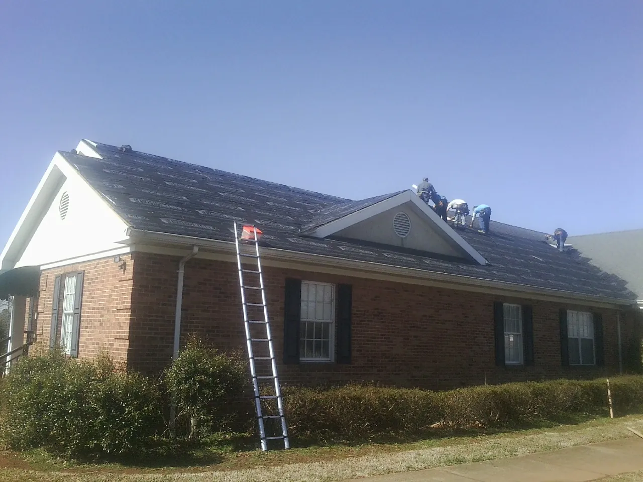 Crew tearing shingles off a brick ranch roof with a ladder set — Metal Roof Repair work by our crew in Bandera