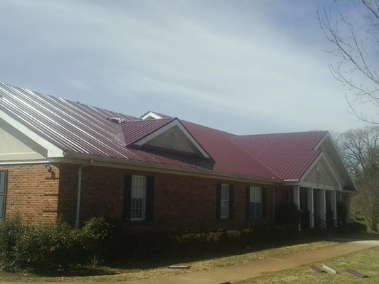 Red metal roof with gabled entries on a long brick building, from a Hail Damage Roof Repair job in Bandera