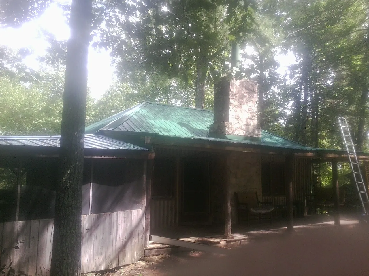Green metal roof and stone chimney above a log cabin porch in Bandera