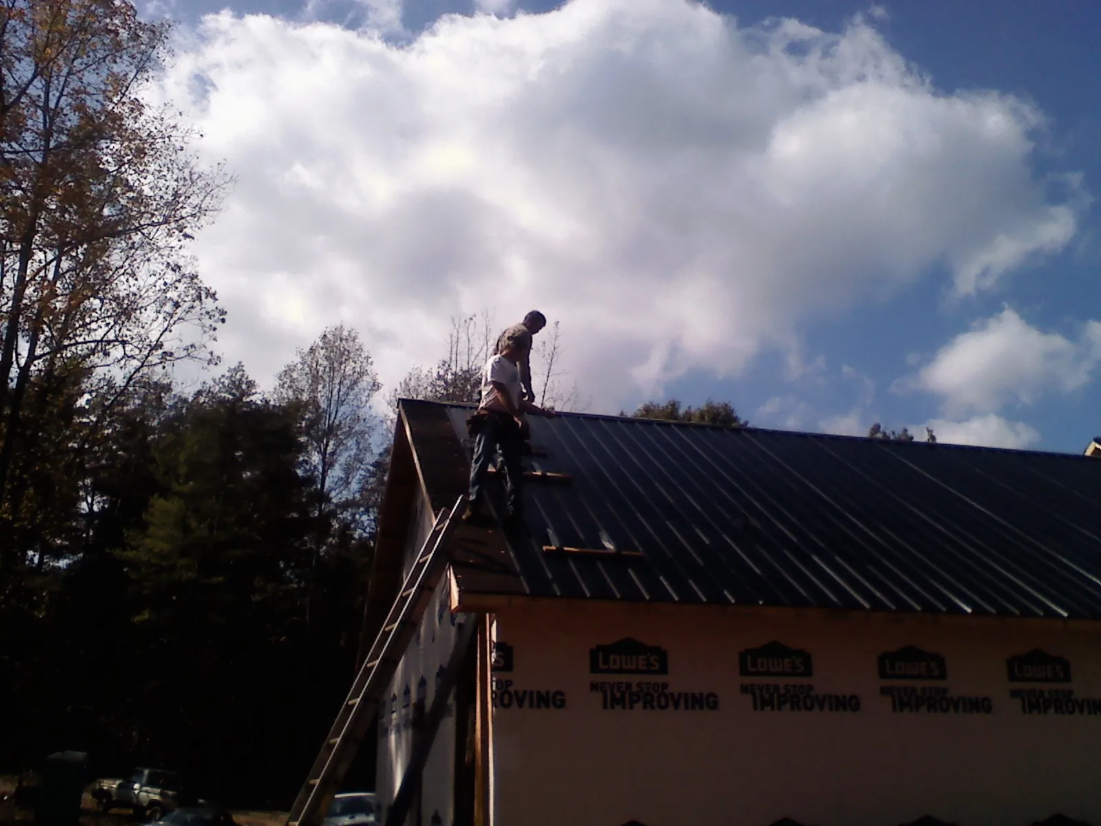 Roofer fastening dark metal panels high against a cloudy sky, from a Roof Inspection job in Bandera