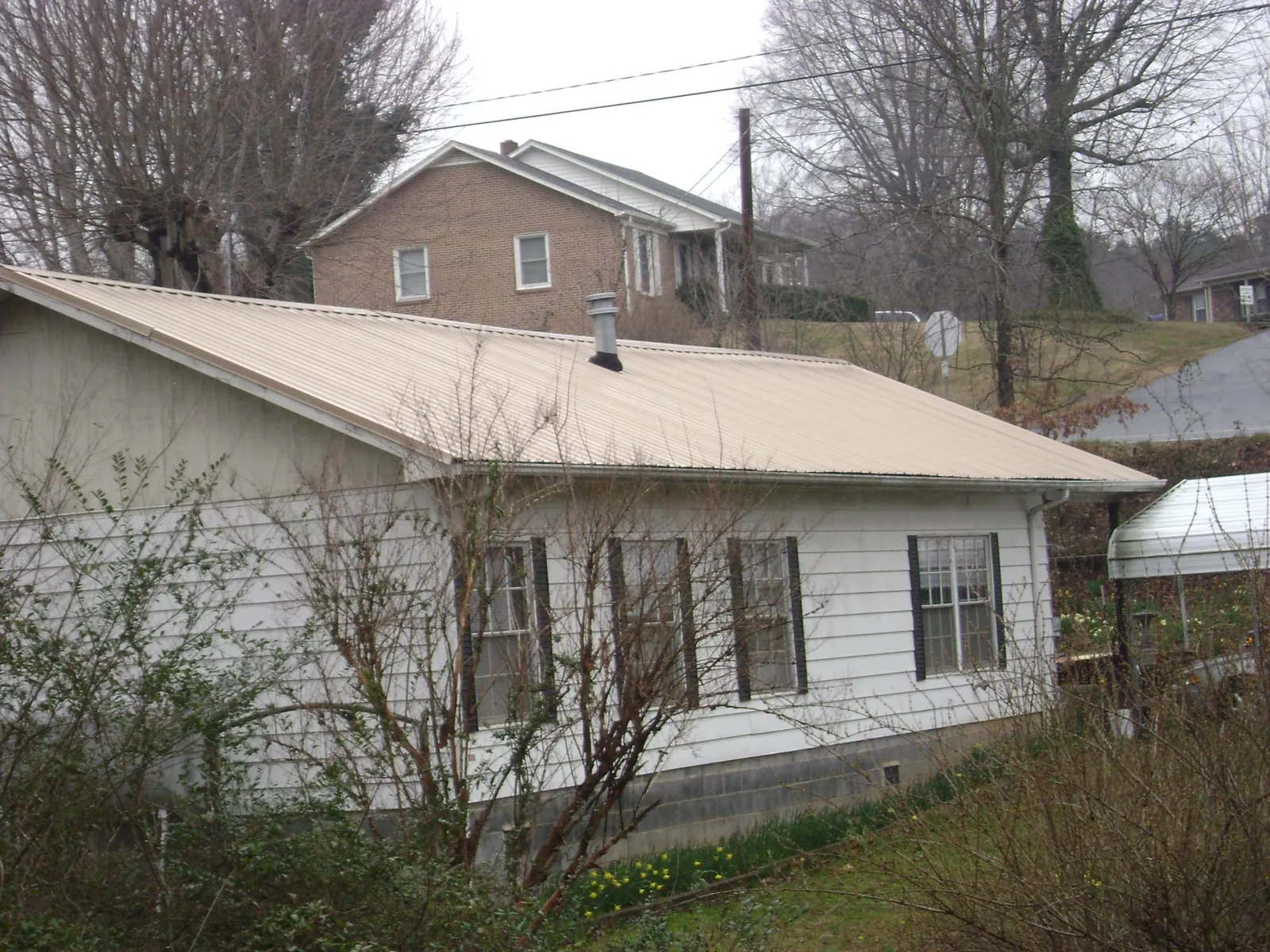 Tan metal roof on a white sided house set into a hillside — Commercial Roofing by Roofing Brothers in Bandera